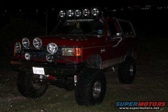 Red Ford Bronco with many lights on roof and bumper, lifted with big tires