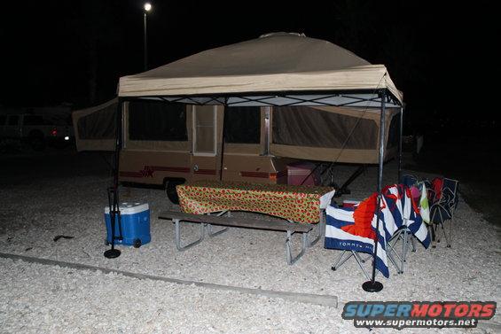 Pop-up camper set up at campsite with picnic table and chairs