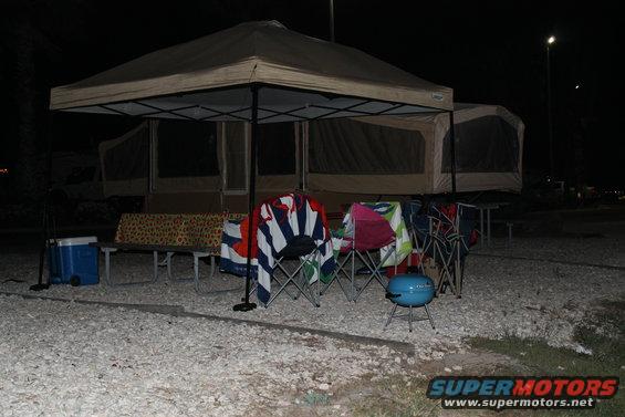 campsite setup at night with pop-up tent, chairs, cooler, and grill