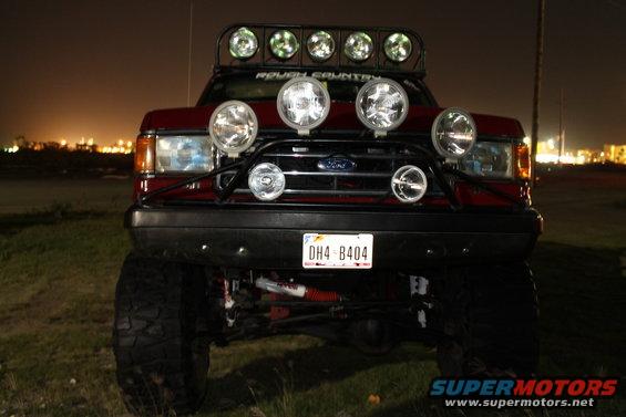 Red Ford truck, front view, with multiple off-road lights and a light bar. License plate DH4-B404