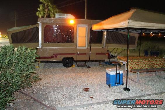 Pop-up camper with awning and cooler at campsite