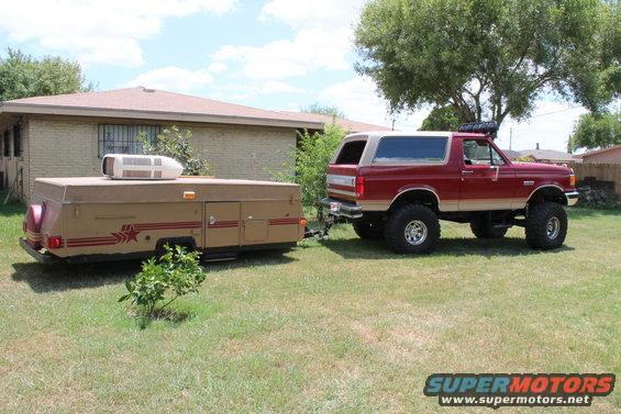 Red and tan lifted 1990 Ford Bronco towing a pop-up camper