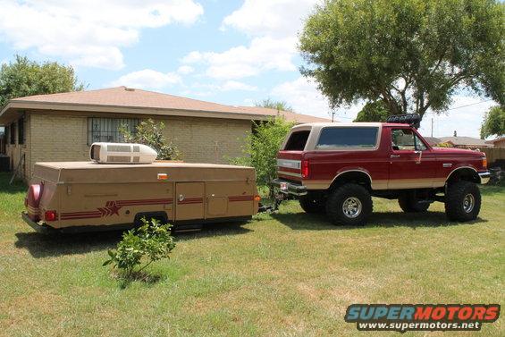 1990 Ford Bronco, lifted, towing a tan pop-up camper in a grassy yard