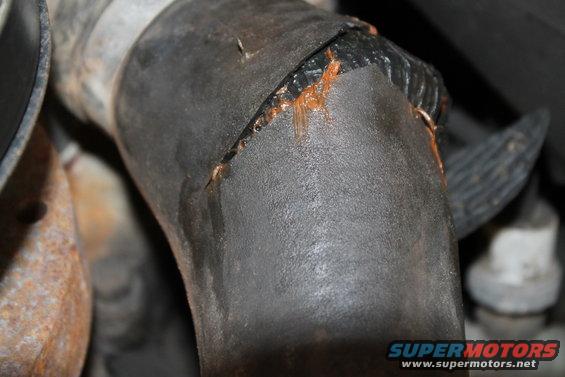 Cracked black rubber hose with orange fluid leaking from the split
