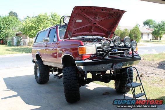 Red lifted Ford Bronco with hood open, extra lights on front. License plate reads OH4-9404