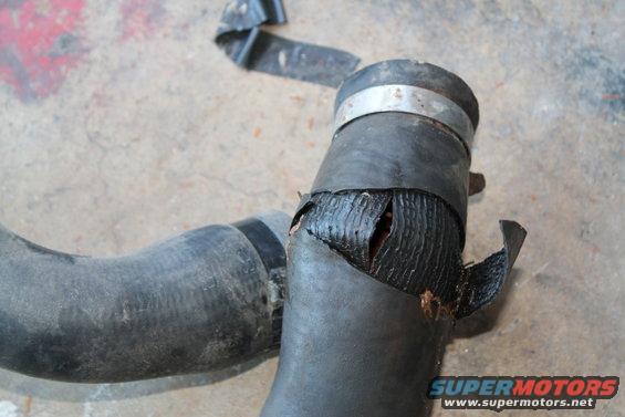 Damaged rubber radiator hose with a large split showing internal reinforcement layers and a metal clamp