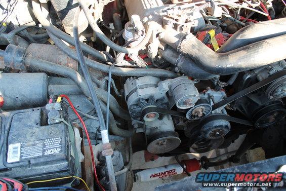 Engine bay with alternator, battery, hoses, and belts visible. Some text on a shock absorber reads 'COUNTRY'
