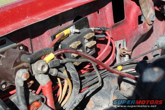 Close-up of a vehicle's engine bay wiring harness and fuse box with red and yellow wires