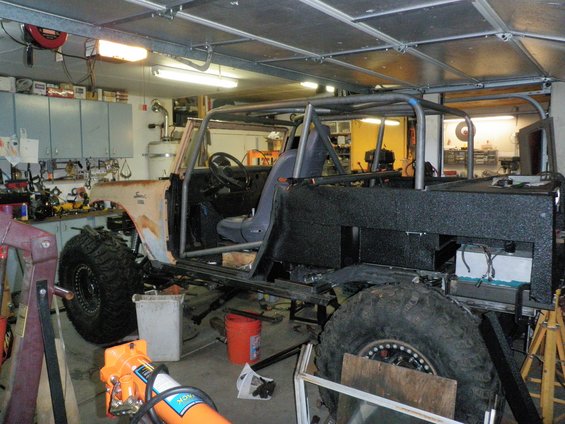 Custom off-road vehicle with roll cage, large tires, and unfinished bodywork in a garage