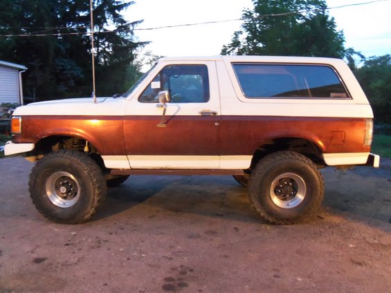 Two-tone brown and white Ford Bronco with lifted suspension and large tires, seen from the side