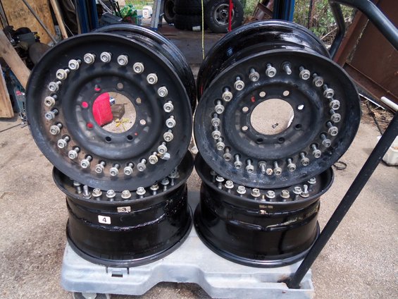 Four black wheels with numerous lug nuts stacked on a dolly