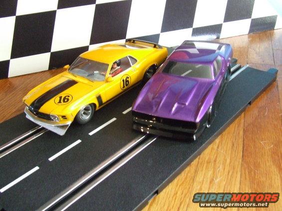 Yellow slot car with black stripes and number 16, next to a purple slot car on a race track