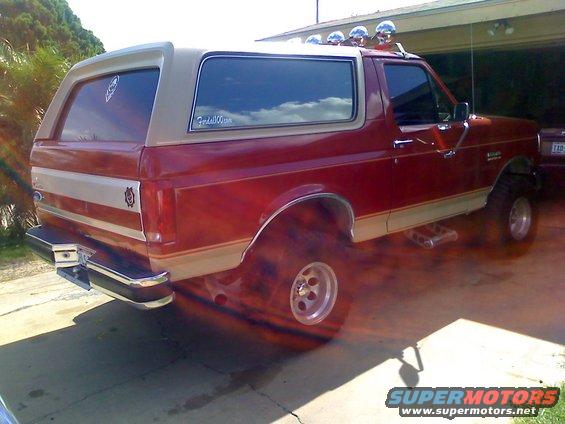 Red and tan Ford Bronco with aftermarket roof lights and side steps, viewed from the rear 3/4 angle