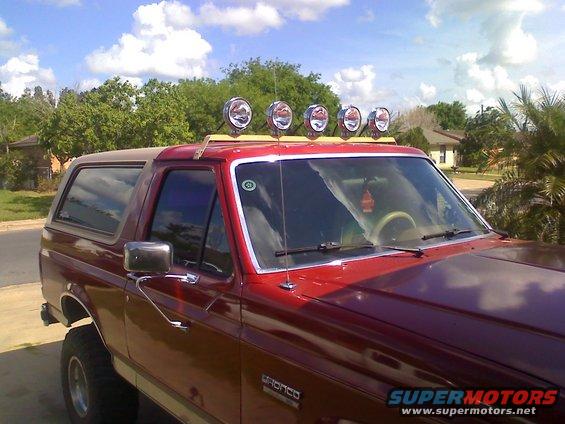 Red 1990 Ford Bronco with four auxiliary lights mounted on a wooden rack above the windshield