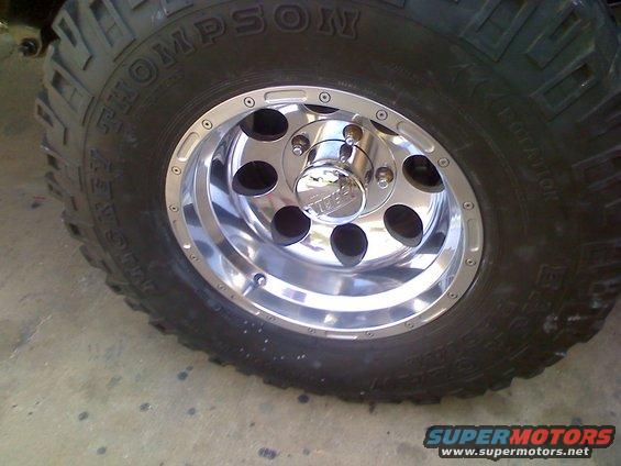 Chrome wheel with black lug nuts and a black tire with 'THOMPSON' text. The wheel has 5 lug holes