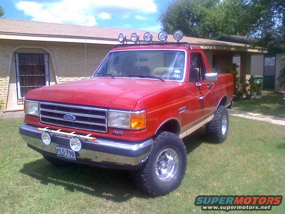 Red Ford pickup truck with off-road lights and lifted suspension parked on grass