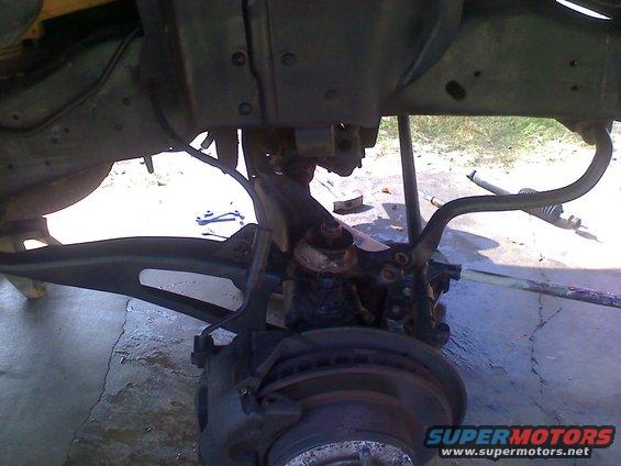 Close-up of vehicle suspension and brake assembly with Supermotors.net watermark
