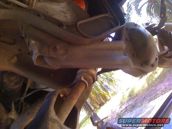 Underside view of vehicle suspension components, showing rust and wear