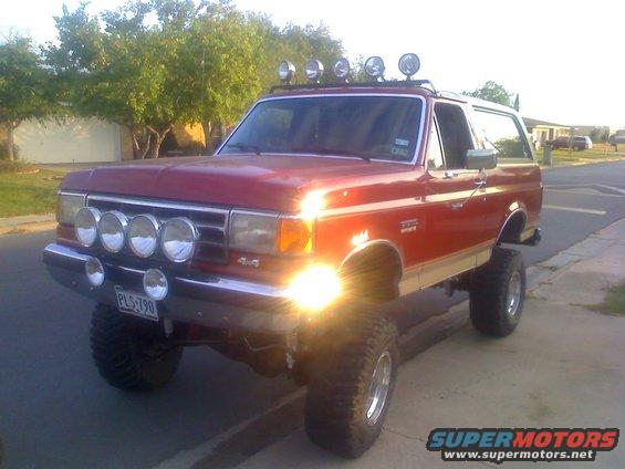Red lifted Ford Bronco with multiple off-road lights on the bumper and roof rack