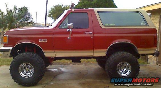 Side view of a red 1990 Ford Bronco with tan trim and large off-road tires