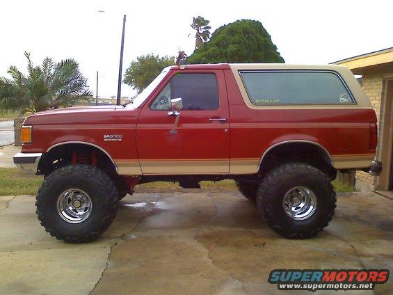 Side view of a red and tan lifted 1990 Ford Bronco with large tires