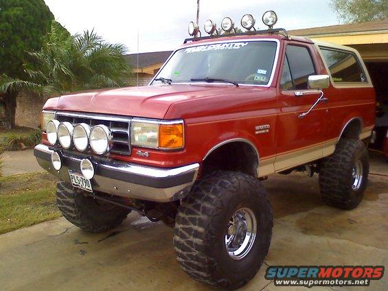 1990 Ford Bronco lifted with large tires and multiple auxiliary lights on front and roof