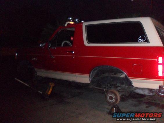 Side view of a red and tan 1990 Ford Bronco on jack stands
