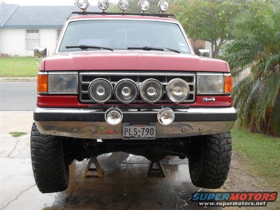 Red Ford truck on jack stands, front view, with roof lights and grille lights. License plate reads PLS 790