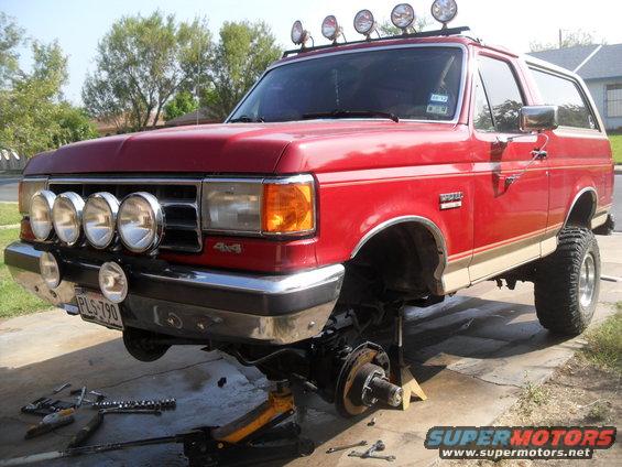 Red Ford Bronco on jack stands with front wheels off, tools scattered around