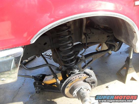 Red vehicle's front suspension with coil spring, brake rotor, and jack stands