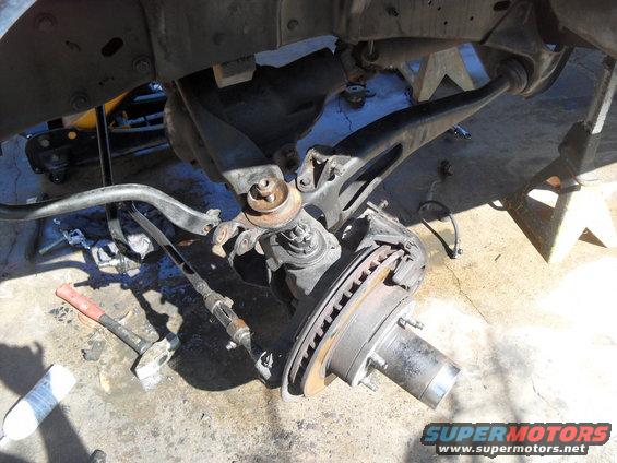 close-up of vehicle's front suspension and brake components, with tools on the ground