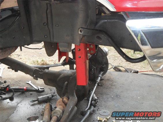 Red vehicle frame with suspension parts and tools on the ground