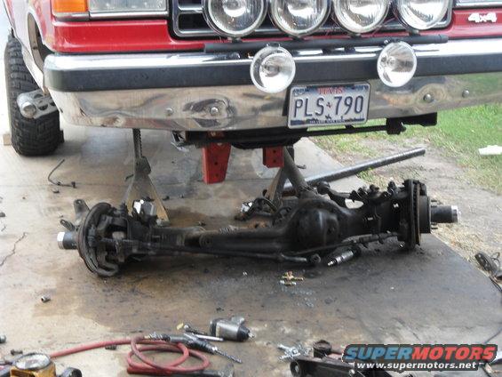 Front axle assembly removed from a red truck, which is on jack stands. Tools and air compressor are on the ground