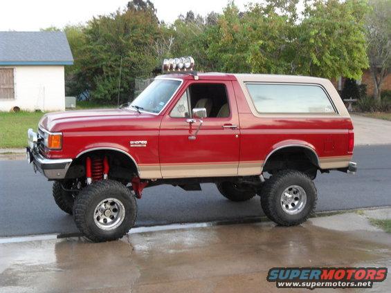 Lifted red Bronco with tan top, off-road tires, and light bar on roof