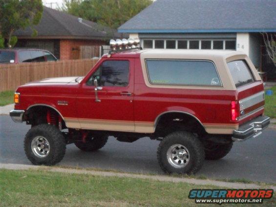 Lifted red Ford Bronco with tan top, parked on street