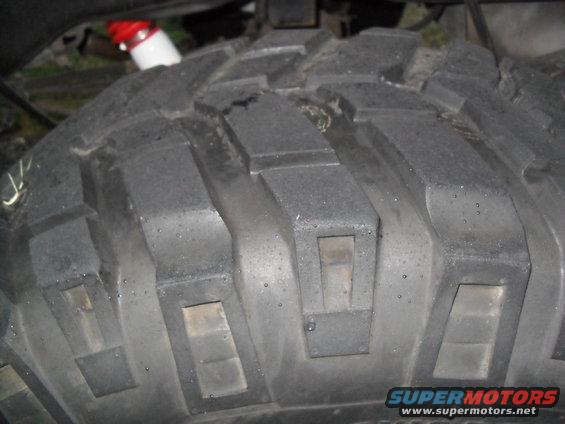 Close-up of a knobby off-road tire tread. Red and white shock absorber visible above