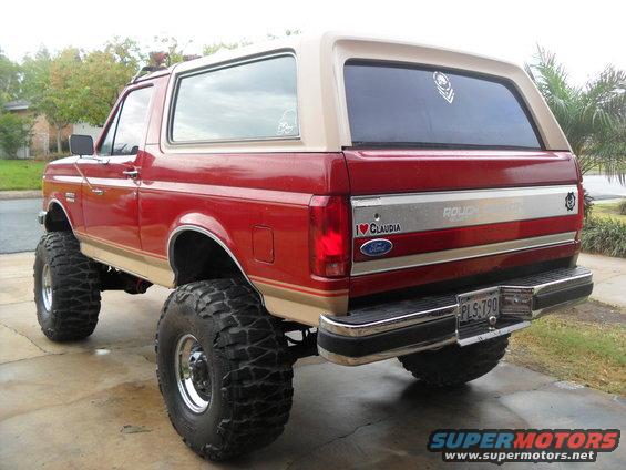 Red and tan 1990 Ford Bronco with lifted suspension and large off-road tires, viewed from the rear