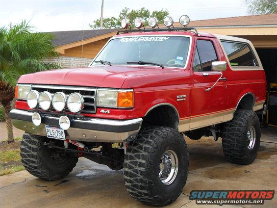 Lifted red 1990 Ford Bronco with off-road lights and "Ranch Country" sticker on windshield