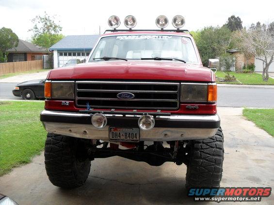 Red Ford F-Series truck with lifted suspension and off-road tires, front view