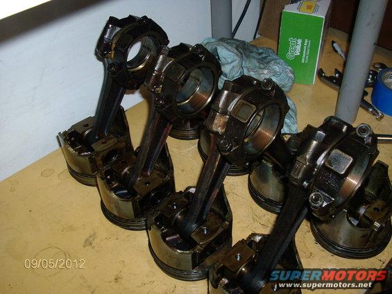 Several engine pistons with connecting rods attached, laid out on a table