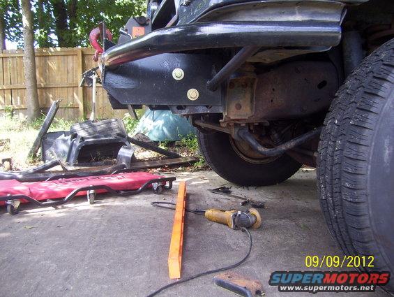 1990 Ford Bronco rear bumper with tow hook, suspension, and tire. Grinding tool on concrete