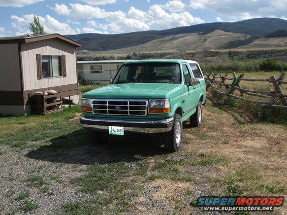 Green Ford Bronco parked in front of a trailer home with mountains in the background