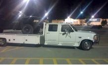 White flatbed truck towing a black SUV at night