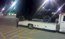 Black SUV being loaded onto a flatbed tow truck at night in a parking lot