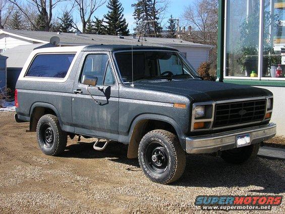 Gray Ford Bronco with a white top and aftermarket wheels parked on a gravel surface