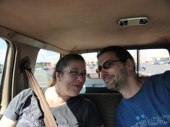 Two people in the interior of a vehicle, looking at each other. A seatbelt is visible