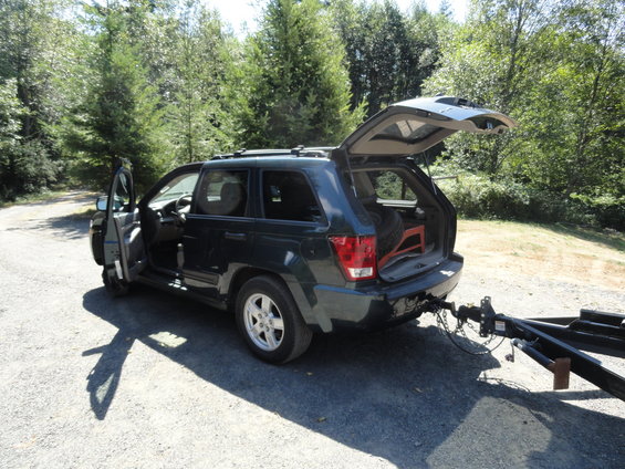 Dark SUV with rear hatch and driver's door open, parked on gravel with a trailer attached