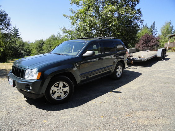 Dark green Jeep Grand Cherokee parked on gravel, hitched to a flatbed trailer