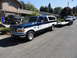 1966 International Scout 800 - A two-tone blue and white Ford F-150 pickup truck, likely from the mid-1990s, is seen towing a car on a trailer.