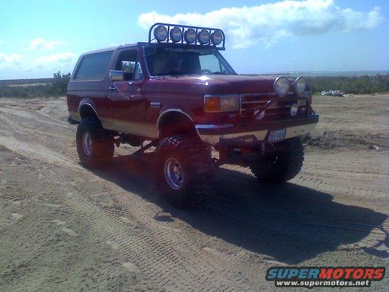 1990 Ford Bronco lifted with off-road lights on roof and bumper, driving on sand